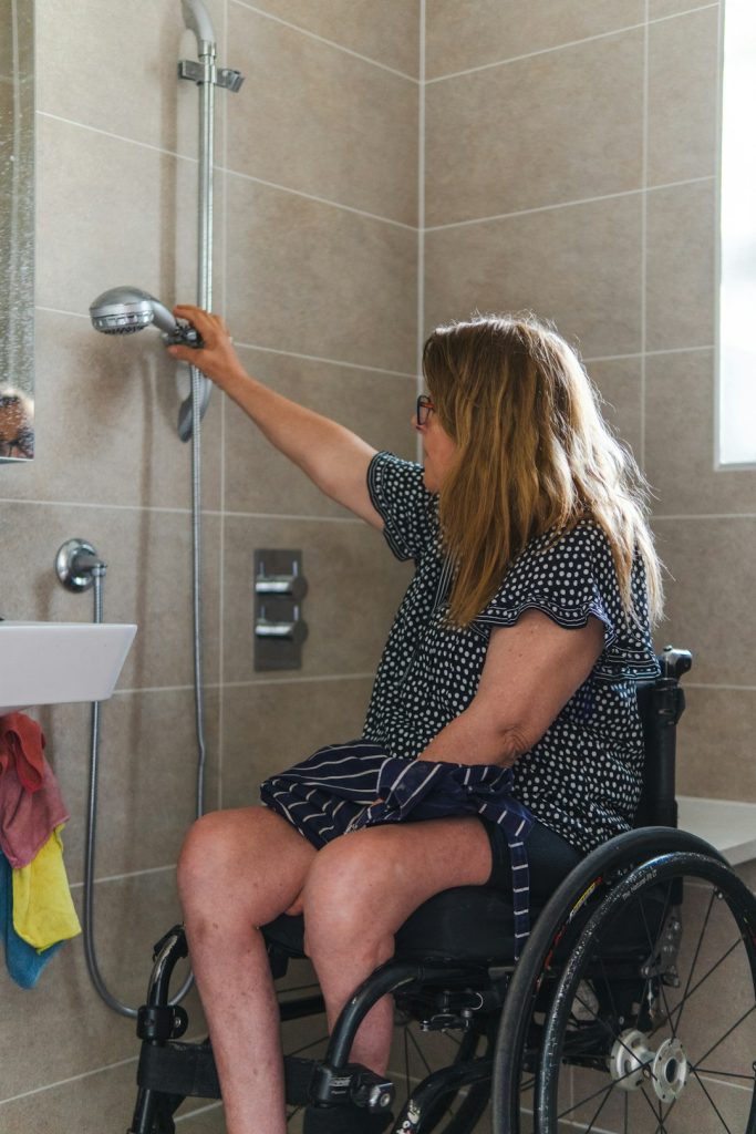 woman-in-wheelchair-using-shower-head-in-accessible-bathroom-d2cxpwtgsgq